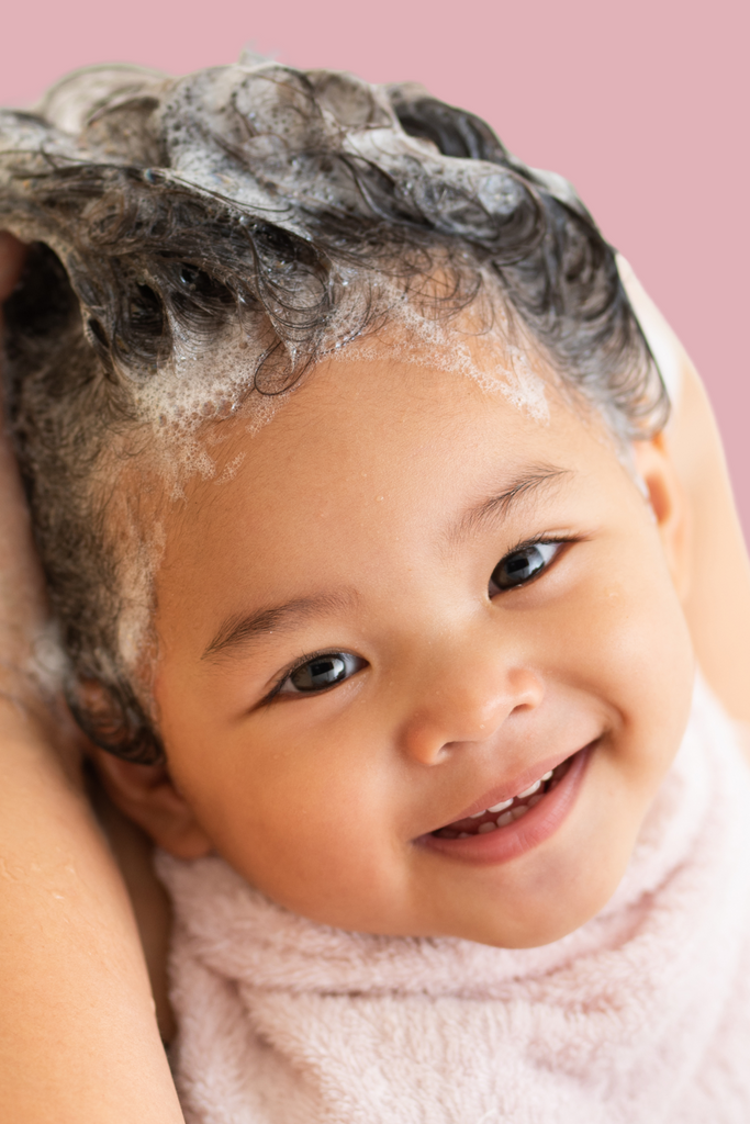 Adorable baby getting hair washed on a pink background.